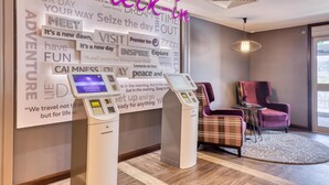 Ein Check-in-Terminal, ein Empfangsbereich mit einer Wand voller inspirierender Zitate, ein violettes Sessel und ein kariierter Sessel.