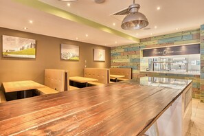 Un restaurant avec des tables et des banquettes en bois, un comptoir avec une vitrine réfrigérée et des œuvres d’art accrochées aux murs.