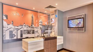 Ein Hotel-Rezeptionsbereich mit einer großen Wandmalerei zum Thema Eis, einem digitalen Bildschirm, der den Hotelnamen anzeigt, und einem Holzboden.