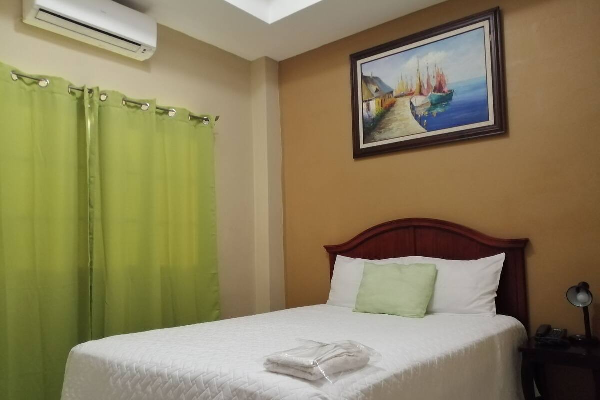Een hotelkamer met een bed, een schilderij van een kustlandschap en een airconditioning.
