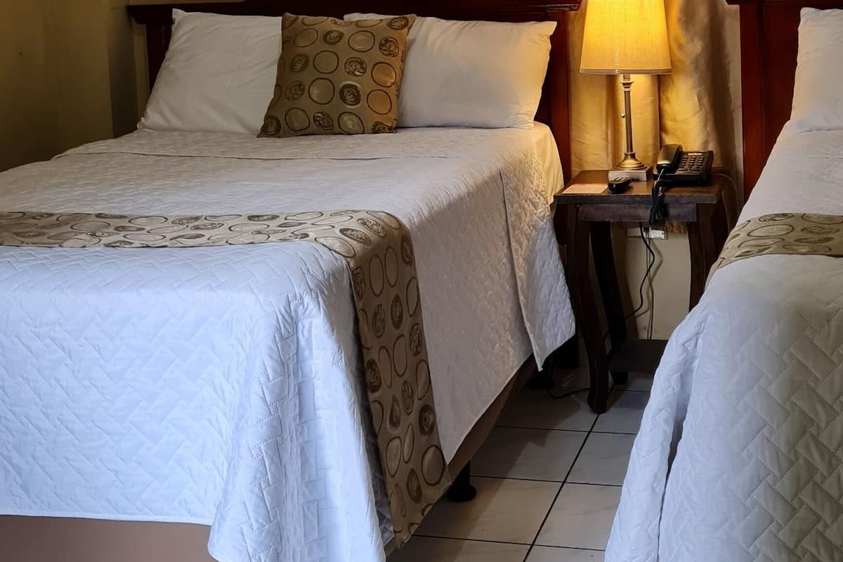 Een hotelkamer met twee bedden, een nachtkastje met een lamp en een wandairconditioner.