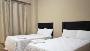 Twee eenpersoonsbedden met witte lakens en donkere hoofdborden in een kamer met beige wanden.