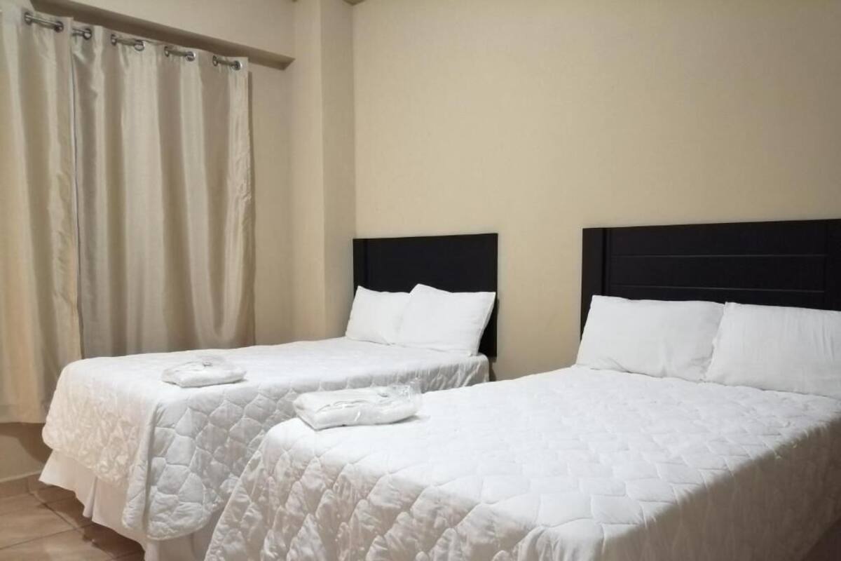 Twee eenpersoonsbedden met witte lakens en donkere hoofdborden in een kamer met beige wanden.