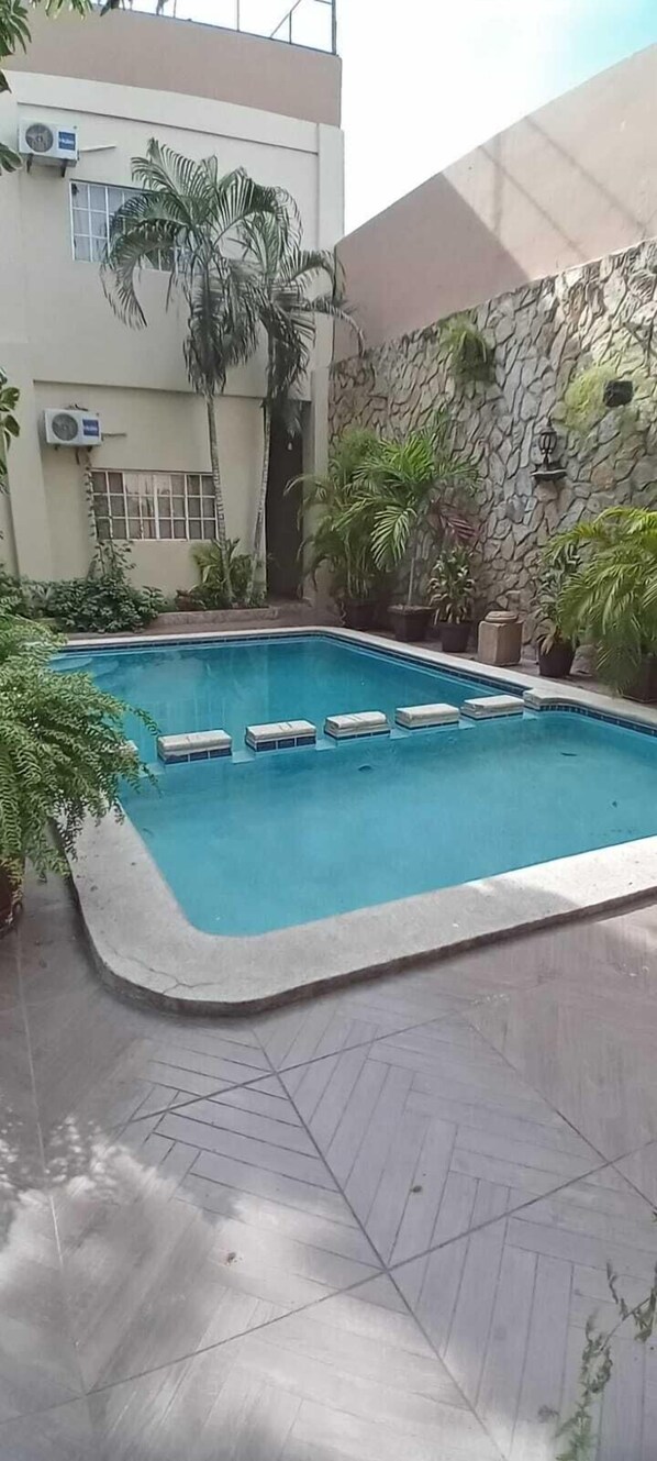 A swimming pool with a stone wall and potted plants around it.