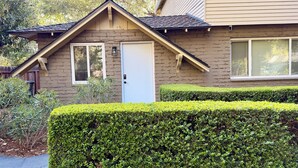 Une maison avec une porte d’entrée, deux fenêtres, un petit porche et une haie bien entretenue.