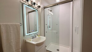 Une salle de bain avec une douche à parois de verre, un lavabo avec un miroir et un porte-serviettes.
