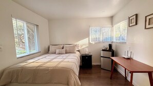 Une chambre à coucher comprenant un lit, une table de chevet, un bureau et un réfrigérateur.