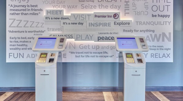 Two self-service kiosks in a hotel lobby with motivational posters and a wooden floor. - Premier Inn Scarborough - North Bay (Scarborough)