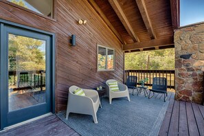 A covered outdoor area with two white chairs and a table, a stone wall, and a wooden deck.