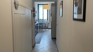 A narrow hallway with a tiled floor, a dining area with a table and chairs, and a kitchen area with cabinets and appliances. - Apartment "Liberty" (Paderno Dugnano)