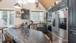 A modern kitchen with a large island, stainless steel appliances, and wooden ceiling beams. - Main Street Tri-plex close to everything! (Telluride)