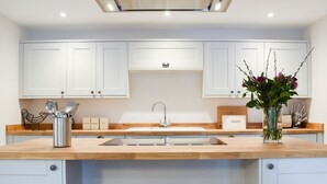A modern kitchen with white cabinets, a central island with stools, and a vase with flowers. - The Old Stables 2 - UK35616 (Winterslow, near Salisbury)