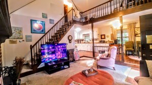A living room with a television, a staircase, and a kitchen in the background. - Make Casa Cabina Your Next Vacation Rental (Henderson)
