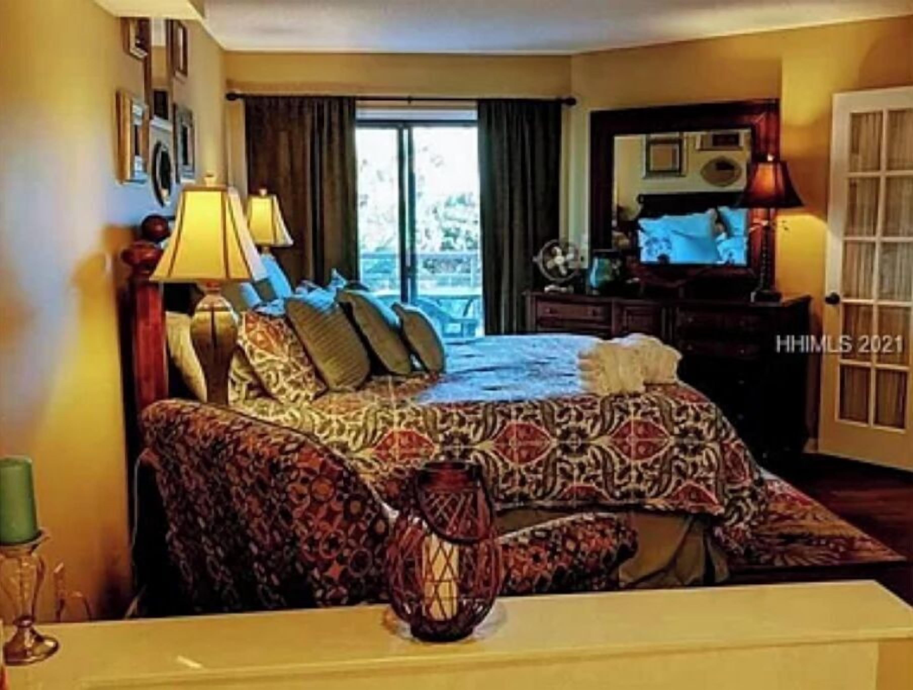 Quarto de hotel com cama, mesa de cabeceira, luminária, cômoda e janela com cortinas.