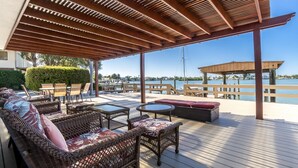 Une terrasse extérieure aménagée avec des meubles en osier, une pergola en bois et une vue sur l’eau.