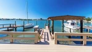 Une jetée en bois mène à une zone d’amarrage pour bateaux, abritée et offrant une vue dégagée sur le port de plaisance et les bâtiments situés au loin.