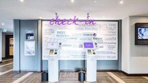 En hotellobby med en incheckningskiosk, en digital skärm och en vägg med inspirerande citat.