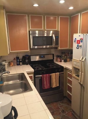 Kitchen area with a gas stove, microwave, refrigerator, double sink, and tiled backsplash.