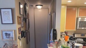 Un couloir étroit, avec un coin cuisine sur la droite, comprenant un réfrigérateur, un four à micro-ondes et divers ustensiles de cuisine.