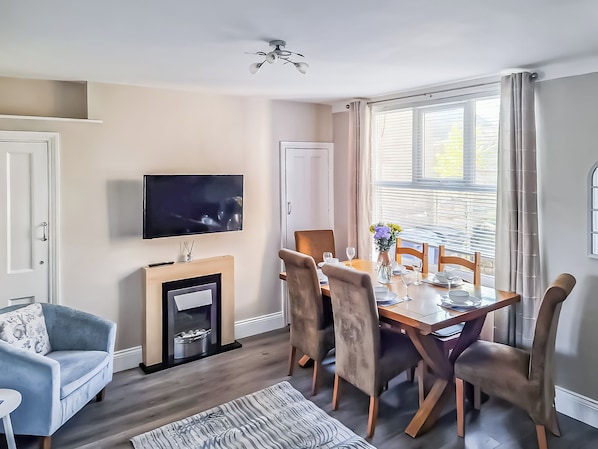 A dining area with a table set for four, a television mounted on the wall, and a fireplace.