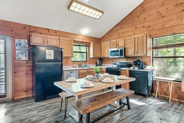 Cocina tipo cabaña de madera con mesa para cuatro, refrigerador, microondas y cafetera.