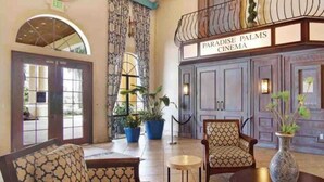 Una hall con divani decorati, un tavolino rotondo, piante in vaso e un cartello per il Paradise Palms Cinema.
