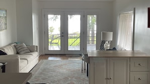 A room with a sofa, a desk, a lamp, and a view of a garden through a sliding door.