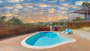 A swimming pool with a wooden deck, a covered seating area, and a view of a cityscape in the background. - The Agave House | Mountain Views & Pool (La Mesa)