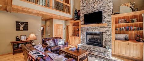 A spacious living room with a stone fireplace, leather sofas, and a wooden staircase.