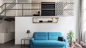 A modern living room with a blue sofa, a small side table, a mirror, and a staircase with a white railing. - New! Trevi Fontain Modern Loft Apartment  (Roma)