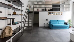 A modern interior with a staircase, a blue sofa, and shelves with various items. - New! Trevi Fontain Modern Loft Apartment  (Roma)