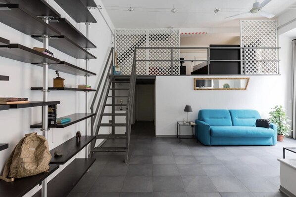 A modern interior with a staircase, a blue sofa, and shelves with various items.