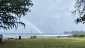 A beach with a grassy area, picnic tables, and a signpost. - Heavenly Hanalei Home in Tropical Paradise (Hanalei)