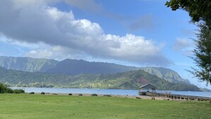 A grassy area with a dock and a small pavilion by a lake, surrounded by mountains. - Heavenly Hanalei Home in Tropical Paradise (Hanalei)