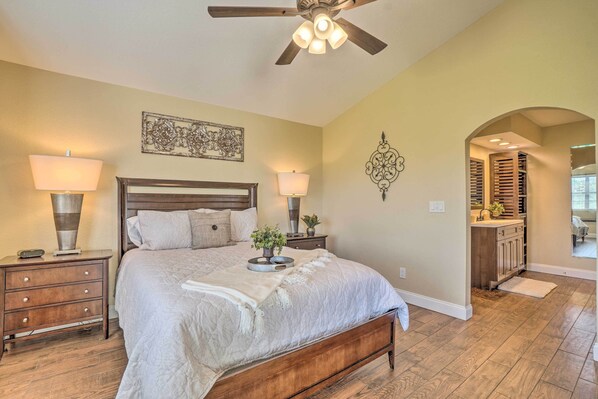A bedroom with a bed, two bedside tables with lamps, a ceiling fan, and a hallway leading to a bathroom. - 1 Block to Branson Strip: Cozy Golf-View Condo (Branson)