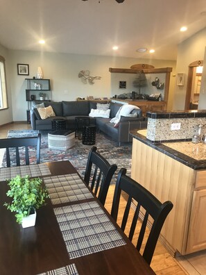 Una sala moderna con un sofá gris oscuro, una mesa de comedor con sillas negras y una zona de cocina con encimeras de granito.
