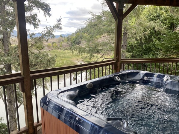 Relax in a hot tub on a deck overlooking a serene landscape with trees and a distant mountain range.