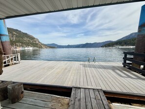 Een houten terras met een metalen hekwerk, met uitzicht op een rustig meer met bergen op de achtergrond.