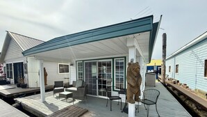 A covered outdoor deck with seating, a bear statue, and a dock. - The Bear Den (Bayview)