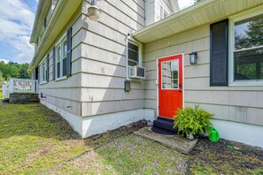 A house with a red door, white siding, and a small front yard with a garden bed and a green watering can.