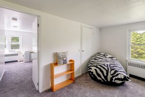 A room with a zebra-patterned bean bag, a wooden shelf with a cushion, a white radiator, and a window with a view of greenery.
