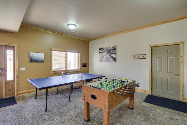 Una habitación con mesa de ping pong, mesa de fútbolín, una puerta y una ventana con persianas.