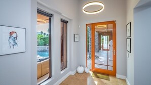 A modern hallway with a glass door leading to a pool area, a framed artwork on the wall, and a circular light fixture above the door. - Luxury Modern Oasis w/ Salt Pool, Spa & Zen Yard (Rancho Mirage)