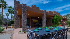 An outdoor patio with a table set for dining, surrounded by stone pillars and palm trees.