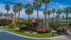 A residential area with palm trees, a well-maintained lawn, and a stone building. - Luxury Modern Oasis w/ Salt Pool, Spa & Zen Yard (Rancho Mirage)