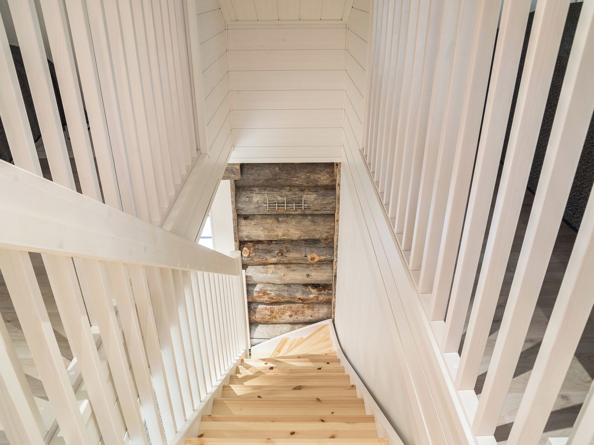 Eine Holztreppe mit Blick auf eine rustikale Blockbauwand im unteren Bereich.
