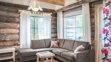 A log cabin interior with a gray sectional sofa, a small wooden coffee table, and a hanging light fixture.