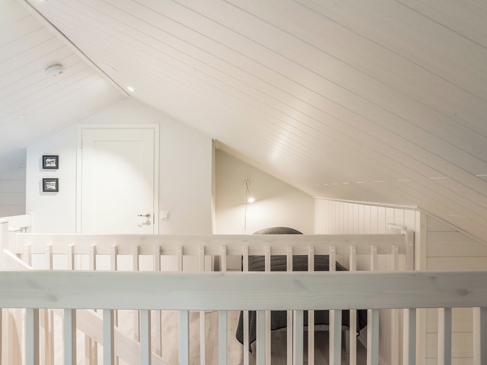 A white interior with a sloped ceiling, a door, and a staircase with a white railing.
