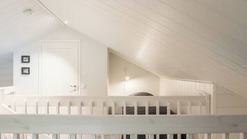 A white interior with a sloped ceiling, a door, and a staircase with a white railing.