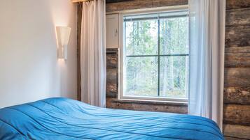 A room with a bed, a window with curtains, and a wall-mounted light fixture.
